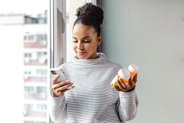 A woman consults with her phone while holding two prescription bottles.